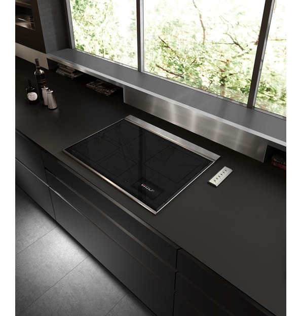 Wolf 30" Transitional Induction Cooktop (CI30460T/S) displayed in a sleek ultra modern kitchen design featuring smooth black countertops, stainless steel backsplash and handleless cabinets 