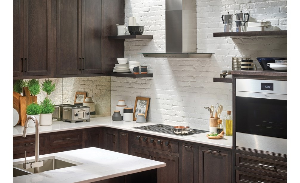 The Wolf 36" Cooktop Wall Hood - Glass (VW36G) shown set against white exposed brick and floating shelves in a luxury kitchen design