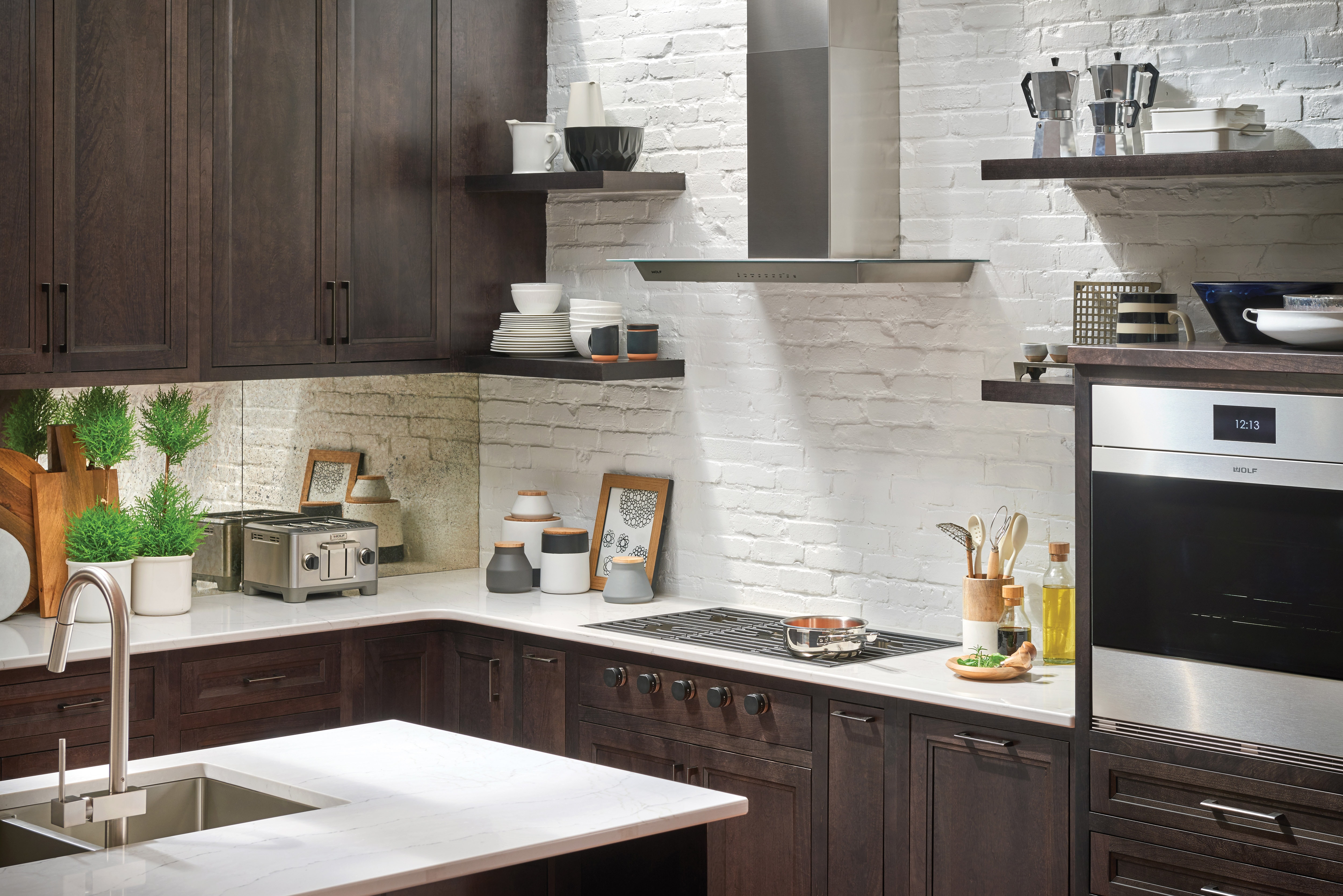 The Wolf 36" Cooktop Wall Hood - Glass (VW36G) shown set against white exposed brick and floating shelves in a luxury kitchen design