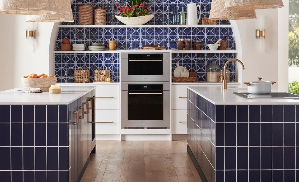 Wolf M Series Transitional Convection Steam Oven (CSO3050TM/S/T) shown in a bright and open Mediterranean kitchen design featuring blue mosaic tile backsplash, white open shelves, pendant lights and gold cabinet handles